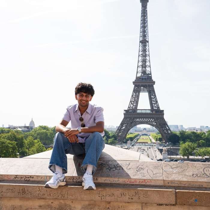 Abhi sitting on a ledge with the Eiffel Tower behind him