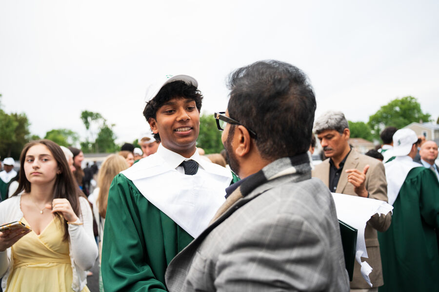 A graduate in a green gown talking with an older man after a commencement ceremony
