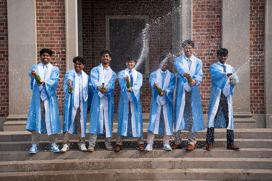 Graduates in light blue gowns spraying champagne on a set of stone steps