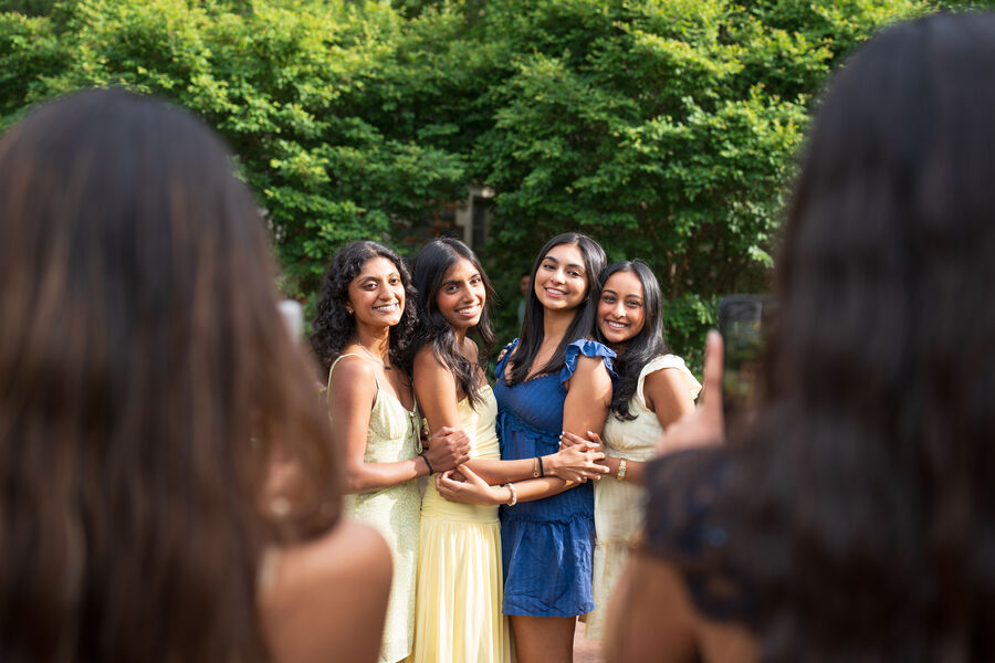 Four friends posing together, seen past a blurred head and a raised phone in the foreground