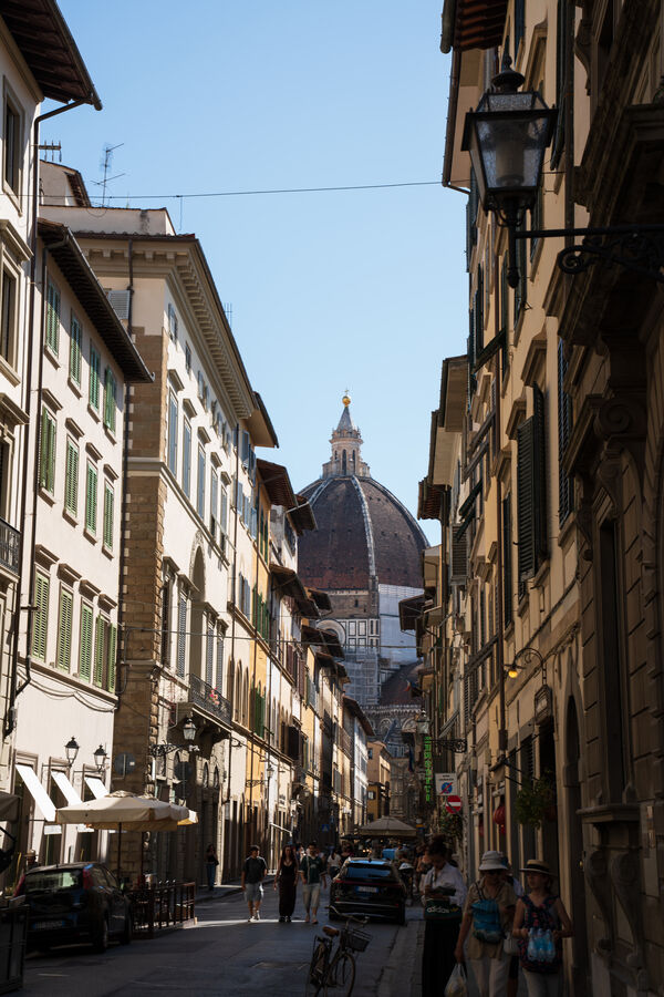A narrow Florence street with the Duomo rising at the far end