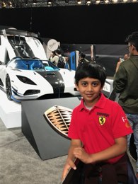 A younger me in a Ferrari polo at a motor show, a white hypercar on the stand behind