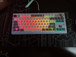 A white Keebmonkey WK870 keyboard lit in rainbow RGB, with a mint coiled cable